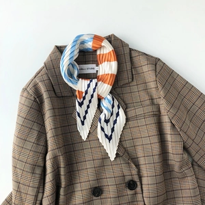 Pleated silk scarf with colorful geometric patterns tied on a brown checkered blazer