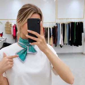 Detail of mint green silk scarf with pink horsebit chain print worn as a neck tie