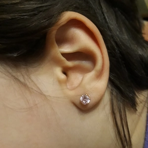 Close-up of pink crystal crown stud earring in gold setting worn on the ear