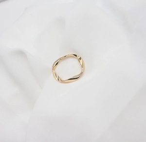 Macro view of golden adjustable ring with twisted wave pattern on soft white fabric