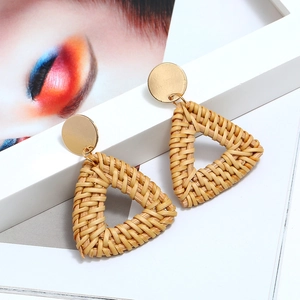 Détail de boucles d'oreilles triangulaires en rotin tressé main avec clous dorés