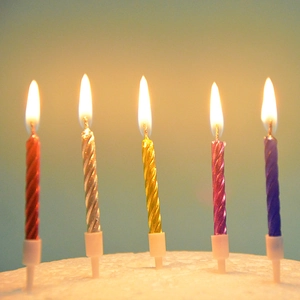 Close-up of five colorful spiral birthday candles with flames and plastic bases