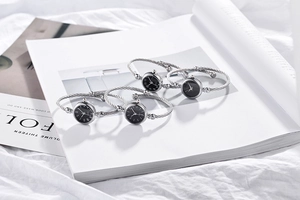 Detail of four silver steel cable bangle watches with black dials on a white magazine