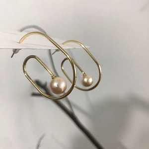 Close-up of golden spiral drop earrings with white pearl detail on a jewelry card