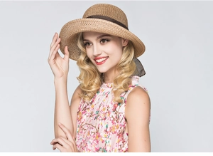 Detail of straw sun hat with dark brown bow ribbon on woman in floral top