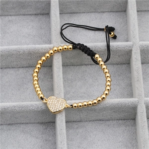 Détail d'un bracelet en perles dorées avec pendentif cœur en zircon et cordon tressé noir