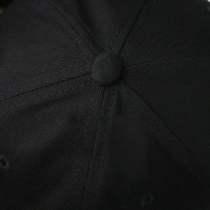 Macro shot of the top button and stitching on a black cotton twill baseball cap