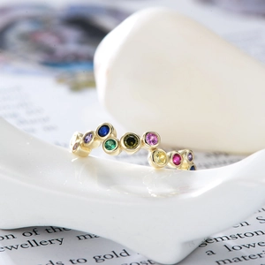 Macro shot of gold wave ring featuring vibrant multi-color zircons on white ceramic base