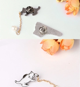 Detail of a white enamel cat brooch and silver pin connected by a gold chain with pearl