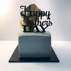 Detailed view of Happy Father's Day black acrylic cake topper on a grey square cake