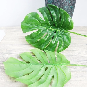 Artificial Monstera leaves in two green tones on a vintage wood grain tabletop