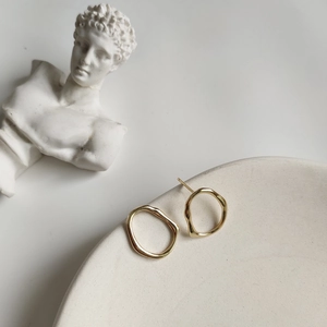 Close-up of gold irregular organic earrings on ceramic tray with minimalist art vibe
