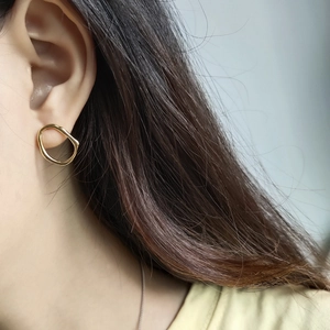 Close-up of irregular hollow golden stud earrings worn on ear showing glossy metallic texture