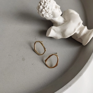 Detailed close-up of gold irregular circular earrings on a textured display tray