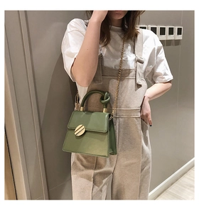 Detail of green crossbody bag featuring a knotted handle and golden circular metal buckle