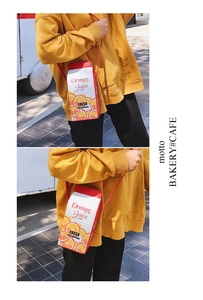 Detail shot of a creative orange juice box shaped crossbody bag with red shoulder strap