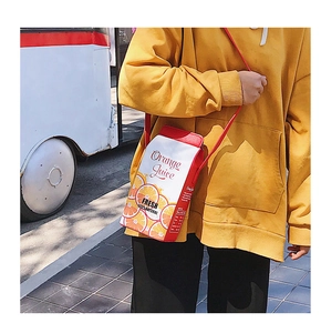 Street style shot of a creative orange juice box shaped crossbody bag in red and white