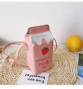 Detail of strawberry milk carton bag with adjustable pink strap on a woven mat