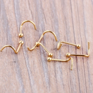 Golden surgical steel nose stud set featuring L-shape screw and bone styles on wood