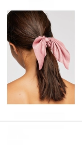 Detailed view of a pink silk-satin bow scrunchie showing fabric texture and long tassels