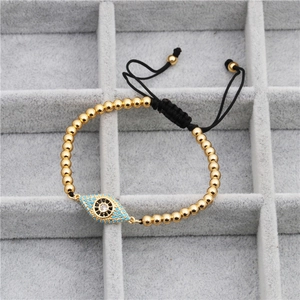 Adjustable golden bead bracelet with evil eye zircon charm on a grey velvet tray