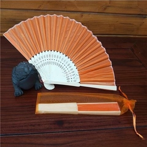 Detail of an orange organza drawstring pouch with a folding fan on wood background