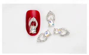 Detailed view of iridescent teardrop crystal nail charm on red manicured nail tips