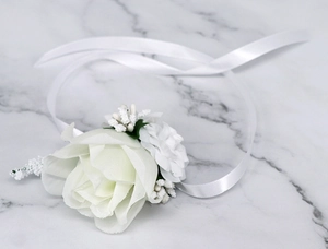 Detail of white artificial rose wrist corsage with berries on white marble background