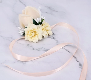 Detail view of a pale yellow silk wrist corsage with champagne ribbon on marble