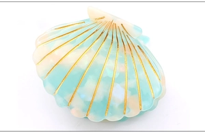 Detailed close-up of shell-shaped hair claw in mint green and ivory acetate with gold lines