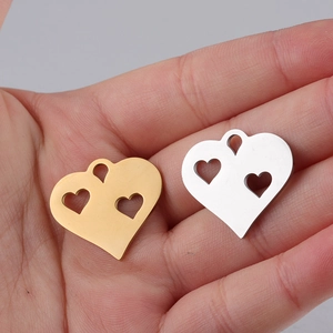 Detailed view of hollow double heart pendants in gold and silver steel on palm