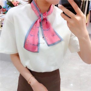Detail of pink silk scarf with gold chain and bit print tied on a white shirt