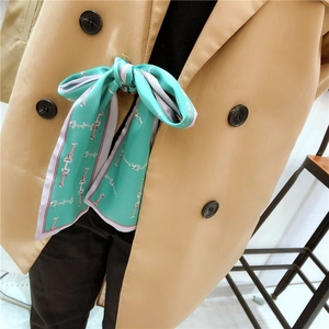 Detail of mint green silk scarf with chain pattern tied on a trench coat neck