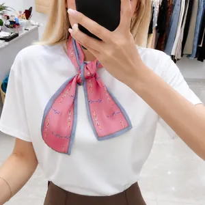 Detail of pink silk ribbon scarf with gold chain print tied in a bow on the neck