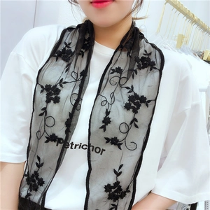 Detail of black lace scarf with floral embroidery and elegant wavy edge on model