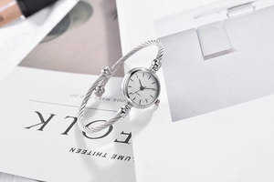 Detail view of a silver minimalist bangle watch featuring a white quartz dial on a magazine