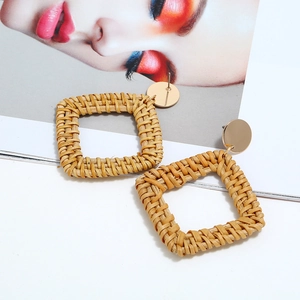 Gros plan de boucles d'oreilles carrées en rotin fait main avec clous dorés sur magazine