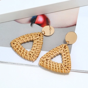 Détail de boucles d'oreilles triangulaires en rotin tressé avec clous dorés sur magazine