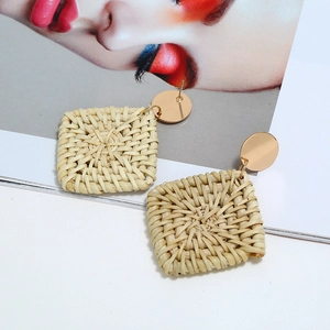 Gros plan de boucles d'oreilles carrées en rotin tressé avec clous dorés sur un magazine