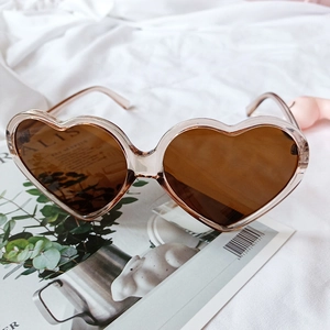 Detail of heart-shaped sunglasses with champagne frame and brown lenses on a magazine