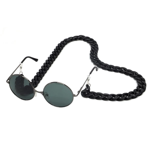 Detail of round black sunglasses with a thick acrylic link chain on a white surface