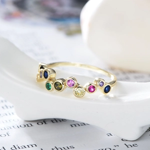 Close-up of wavy gold ring band set with multi-colored circular cubic zirconia gemstones