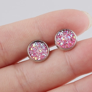 Close-up of 8mm round pink glitter stud earrings held between fingers for size reference
