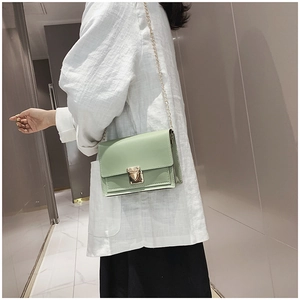 Détail d'un petit sac carré vert clair avec fermoir doré et bandoulière en chaîne dorée