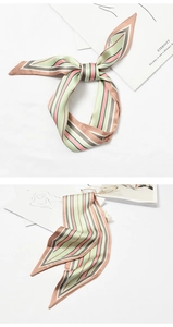 Detail of a pink and green striped silk scarf styled in a bow with elegant accessories
