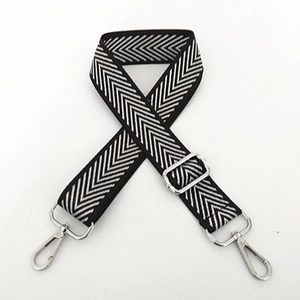 Detail of black and white herringbone nylon bag strap with silver metal hooks and buckles