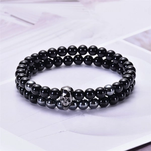 Dettaglio di braccialetti in ematite e onice con un ciondolo a teschio metallico