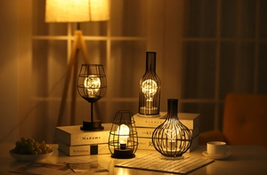 Detail of assorted black iron lamps with warm LED strings on a wooden table surface
