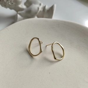 Close-up of golden irregular hollow earrings on a ceramic dish with soft lighting