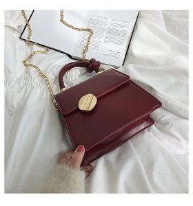 Detail of burgundy leather handbag with twisted handle and gold buckle decoration